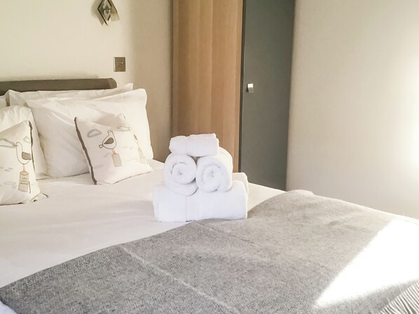 A neatly made bed with rolled towels and decorative pillows, a grey carpet, and a wooden headboard.