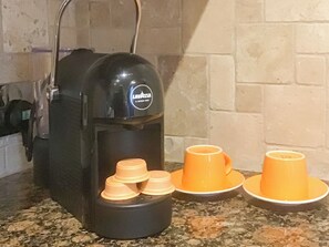 A coffee machine with two orange cups on a granite countertop.