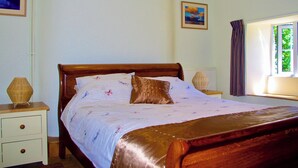 Ein ordentlich bezogenes Bett mit floralem Überwurf, einem Holzkopfende und zwei Nachttischlampen.