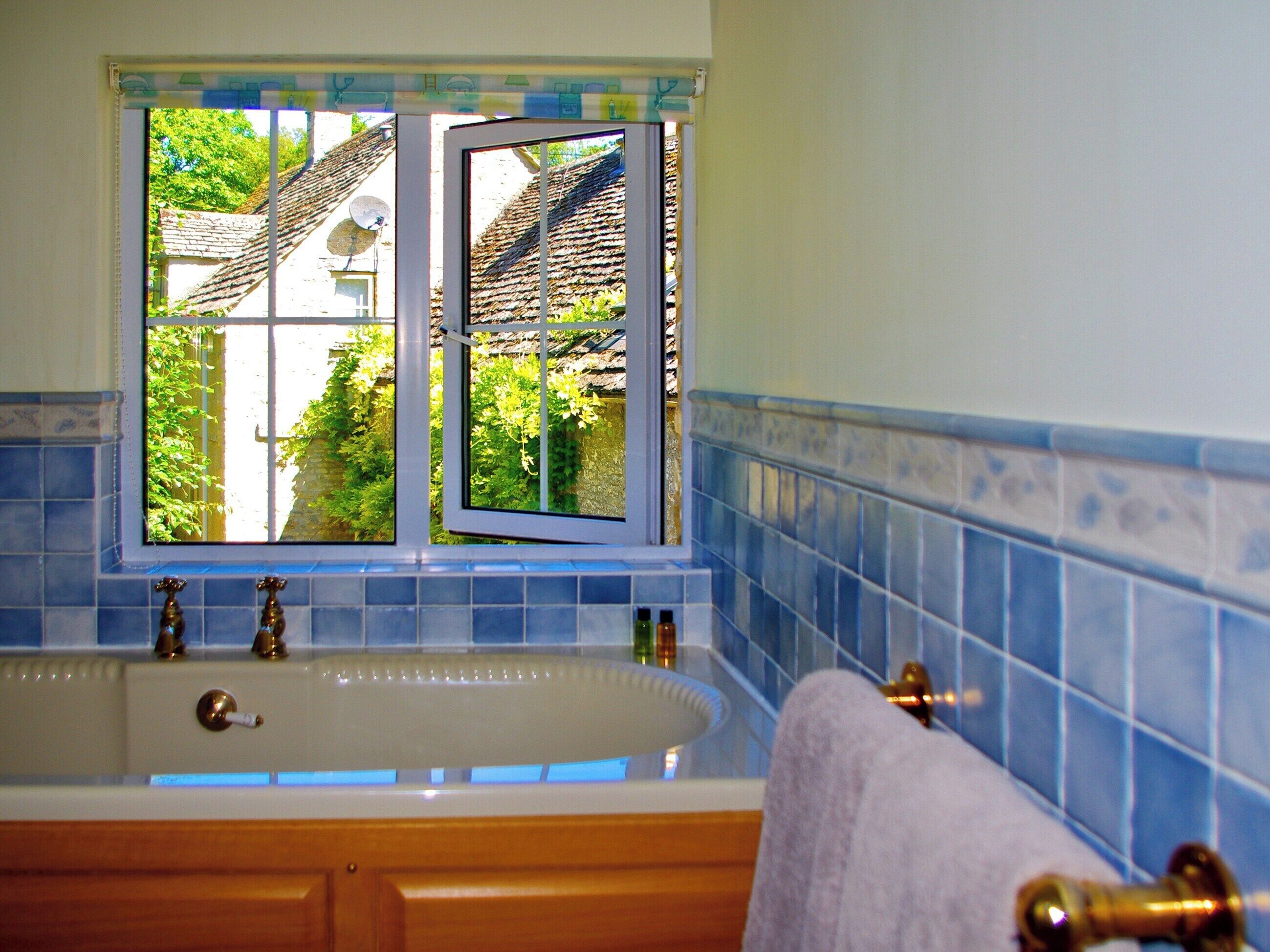 A bathroom with a bathtub, a window with a view of a house, and blue-tiled walls.