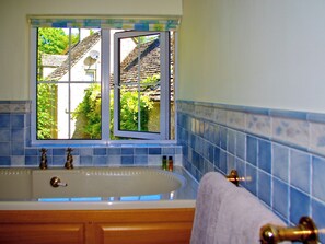 A bathroom with a bathtub, a window with a view of a house, and blue-tiled walls. - 1 bedroom accommodation in Chedworth, near Cheltenham (Chedworth, near Cheltenham)
