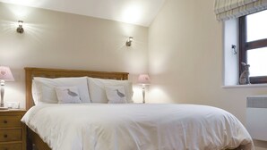 A bedroom with a wooden bed, white bedding, two bedside lamps, a window with a curtain, and a wall-mounted heater. - 1 bedroom accommodation in near Middleham, Leyburn (near Middleham, Leyburn)