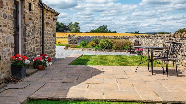 A stone building with a patio area featuring a table and chairs, surrounded by a well-maintained lawn and garden. - 1 bedroom accommodation in near Middleham, Leyburn (near Middleham, Leyburn)