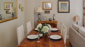 A dining room with a wooden table set for four, surrounded by white chairs. There is a chandelier above the table, and framed artwork on the walls. - 2 bedroom accommodation in Whitby (Whitby)