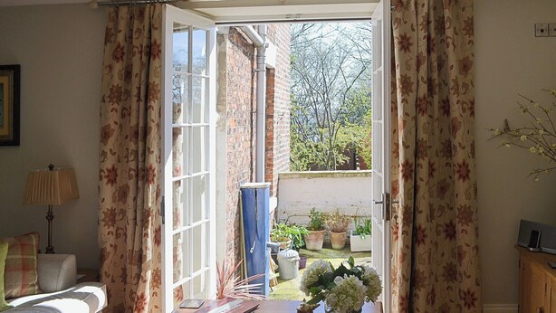 An open door leading to a garden with potted plants, a table with books and a vase of flowers, and a sofa in the room. - 2 bedroom accommodation in Whitby (Whitby)