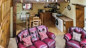 A living room with a red leather sofa and armchair, a wooden dining table, and a kitchen area with a washing machine. - 2 bedroom accommodation in Newton Reigny (Newton Reigny)