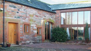 A stone building with a wooden door, arched windows, and a large glass door. - 2 bedroom accommodation in Newton Reigny (Newton Reigny)