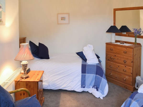 A neatly arranged bedroom with a bed, a wooden dresser, a lamp, and a framed picture on the wall. - 3 bedroom accommodation in Padstow (Padstow)