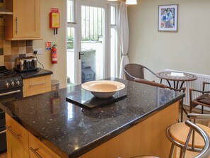 A kitchen with a large island, wooden cabinets, a gas stove, and a dining area with wicker chairs and a small table. - 3 bedroom accommodation in Padstow (Padstow)