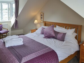 A neatly made bed with a wooden headboard, a bedside table with a lamp, and a chair with a purple cushion. - 3 bedroom accommodation in Padstow (Padstow)