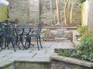 An outdoor patio with a stone wall, a stone bench, and a metal table and chairs.