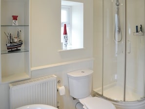 A bathroom with a toilet, a glass-enclosed shower, a radiator, and a shelf with a ship model.
