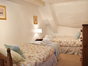 Quarto com duas camas, mesa de cabeceira com abajur e cômoda.