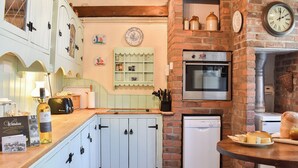 A kitchen with white cabinetry, a Bosch dishwasher, a brick wall, and a clock.