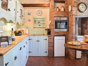 A kitchen with white cabinets, a Bosch dishwasher, a brick wall, and a clock.