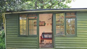 A small, green wooden structure with multiple windows, a bench inside, and a clock on the wall.