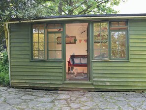 Una pequeña estructura de madera verde con varias ventanas, un banco en el interior y un reloj en la pared.