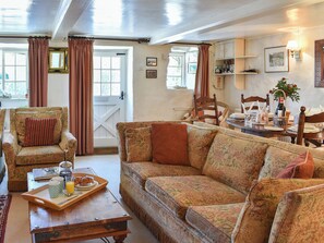 A cozy living room with a patterned sofa, a wooden armchair, and a dining table set for breakfast. - Tranquillity Cottage (Winfrith Newburgh)