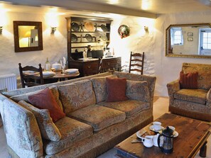 A cozy living room with a patterned sofa, a wooden coffee table with breakfast items, and a wall-mounted shelf with dishes.