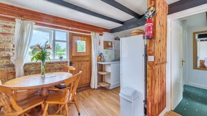 Une cuisine avec des poutres en bois, une table à manger avec des chaises, une fenêtre avec des rideaux et un réfrigérateur blanc.
