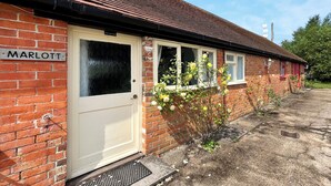 Un bâtiment en briques avec une porte blanche, une plaque portant le nom « MARLOTT », et un petit jardin avec des fleurs jaunes.