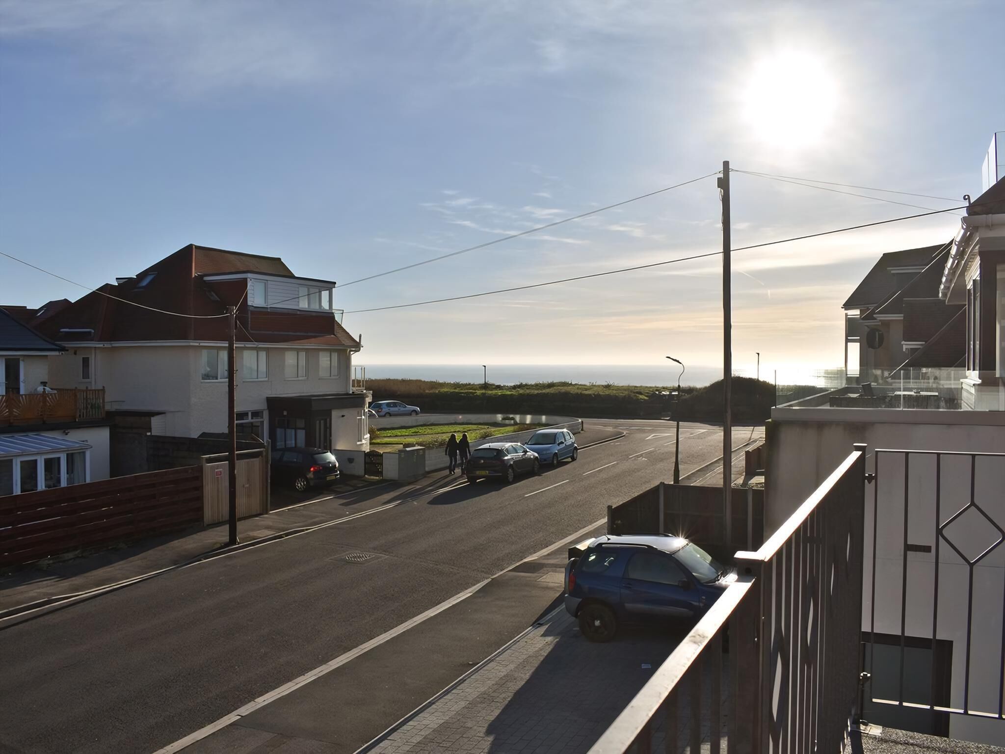 Une rue résidentielle bordée de maisons, avec des voitures garées et un ciel dégagé.
