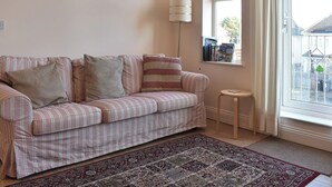Un sofá a rayas con almohadones, una lámpara de pie, una mesita y una alfombra estampada en una habitación con ventanal.