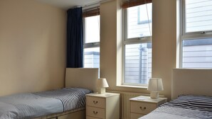 Un dormitorio con dos camas, una ventana con persianas, un radiador y una mesita de noche con lámpara.