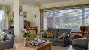 Ein Wohnzimmer mit Couchtisch aus Holz, zwei Sofas, einem Klavier und einem Fenster mit Jalousien.