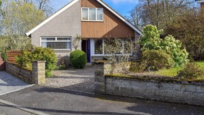 Ein zweigeschossiges Haus mit geneigtem Dach, einer Veranda und einer Auffahrt mit Kies.