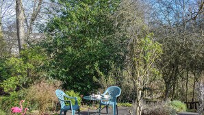 Eine Terrasse mit zwei blauen Stühlen und einem Tisch, umgeben von Bäumen und einem rosa Flamingo.
