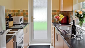 A kitchen with a microwave, stove, sink, and a bowl of fruit on the counter. - 3 bedroom accommodation in Liskeard (Liskeard)