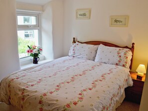 A bedroom with a bed, a window with flowers, and two framed pictures on the wall.