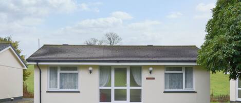 A single-story house with a tiled roof, a front door, and two windows with curtains.