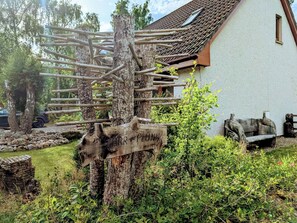 A rustic wooden signpost with directional arrows, a white building with a tiled roof, and a garden with various plants and a bench. - 3 bedroom accommodation in Carrbridge (Carrbridge)