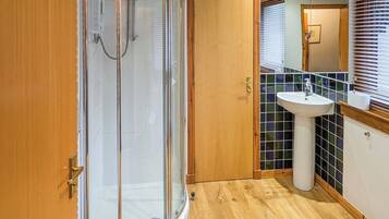 A modern bathroom with a glass-enclosed shower, a wooden door, a sink with a mirror, and tiled walls.