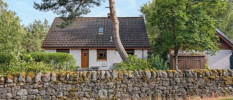 A traditional stone-walled house with a tiled roof, a wooden door, and a small window.