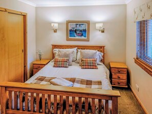 A bedroom with a wooden bed, two bedside tables, a nightstand, a window with blinds, and a wall-mounted painting. - 3 bedroom accommodation in Carrbridge (Carrbridge)