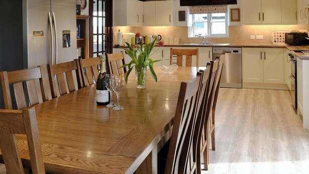 A modern kitchen with wooden cabinets, a dining table set for six, and a built-in dishwasher. - 4 bedroom accommodation in Bradworthy, near Hartland (Bradworthy, near Hartland)