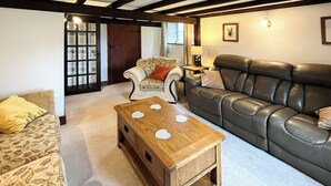 A living room with a floral sofa, a leather sofa, and a wooden coffee table. - 4 bedroom accommodation in Bradworthy, near Hartland (Bradworthy, near Hartland)