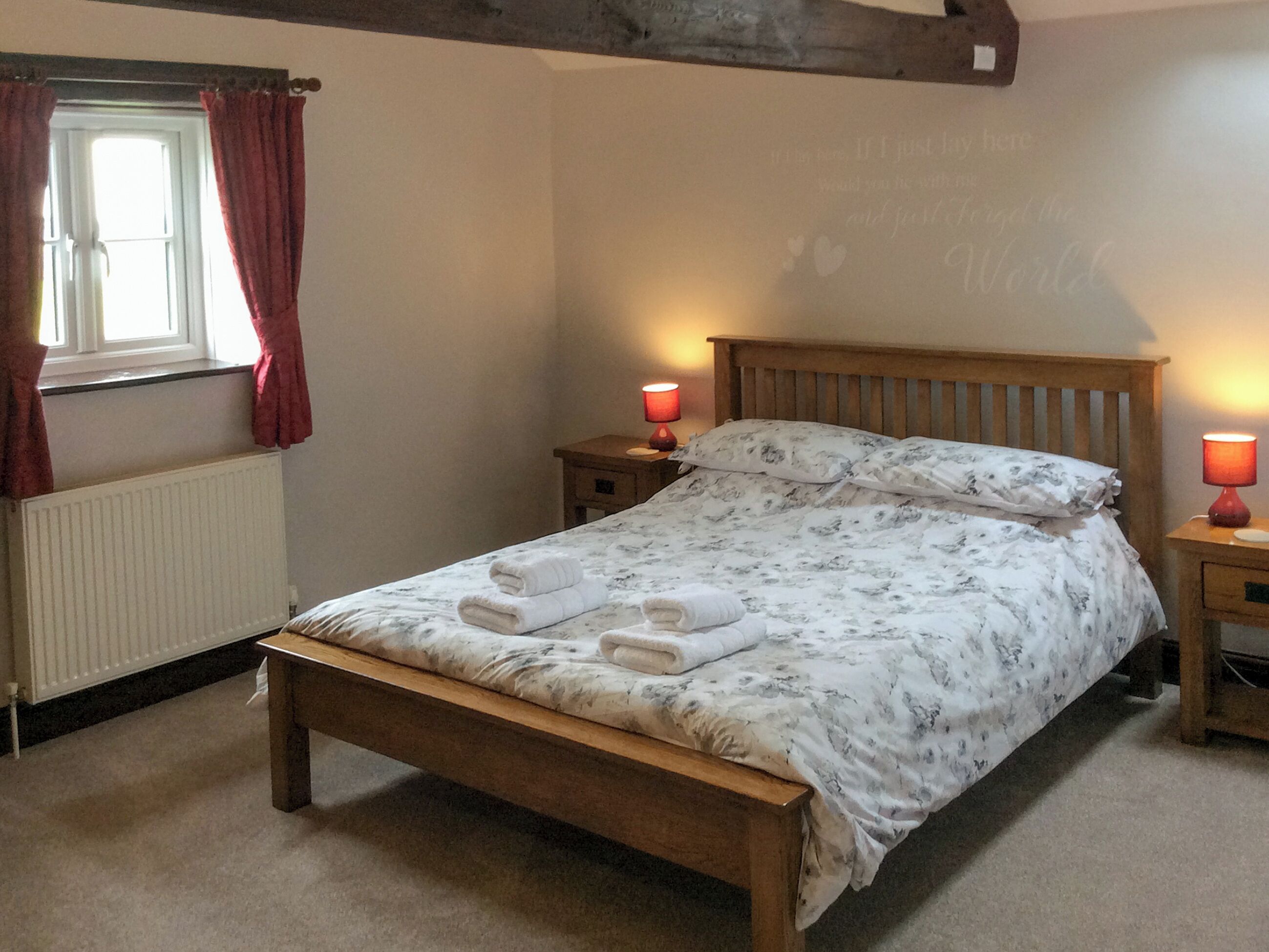 Una camera da letto con un letto in legno, due comodini con lampade, un termosifone e una finestra con tende rosse.