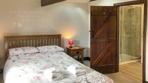 A bedroom with a wooden bed, floral bedding, a bedside lamp, and a large wooden door leading to a shower area. - 4 bedroom accommodation in Bradworthy, near Hartland (Bradworthy, near Hartland)