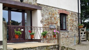 A stone building with a wooden porch, potted plants, and a sign reading "COWSLIP". - 4 bedroom accommodation in Bradworthy, near Hartland (Bradworthy, near Hartland)