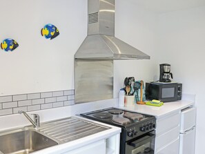 Une cuisine équipée d’un évier, d’une cuisinière et d’un four à micro-ondes en acier inoxydable, ainsi que d’une machine à café et d’ustensiles de cuisine.