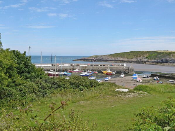 A coastal marina with boats docked, a lighthouse in the background, and a grassy area in the foreground.