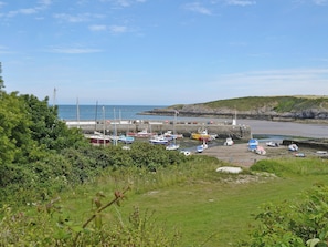 Un port de plaisance sur la côte, avec des bateaux amarrés, un phare en arrière-plan et une zone herbeuse au premier plan.