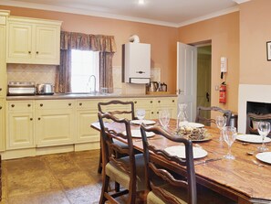 Comedor con una mesa de madera preparada para cuatro personas, cocina con armarios amarillo claro y una chimenea.