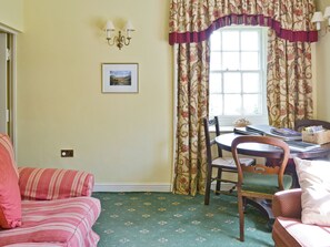 A room with a striped sofa, a dining table with chairs, a chandelier, and floral curtains.