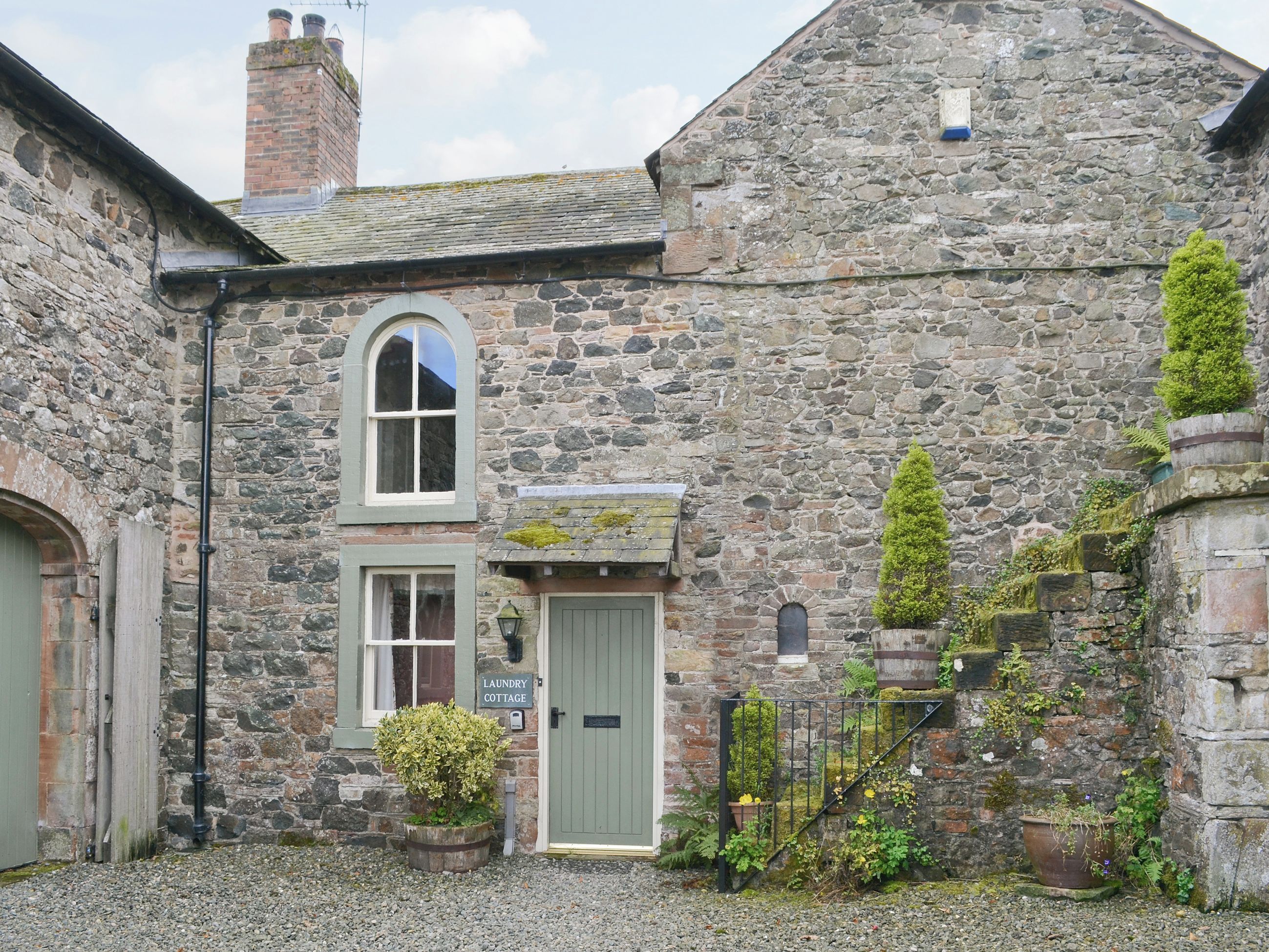 A stone building with a laundry cottage sign, a green door, and a small garden with potted plants.