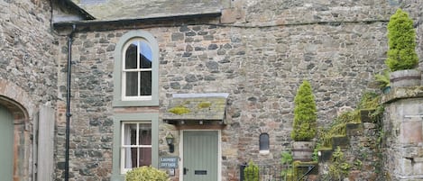 A stone building with a laundry cottage sign, a green door, and a small garden with potted plants.